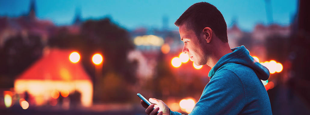 Um homem olhando seu celular ao por do sol.